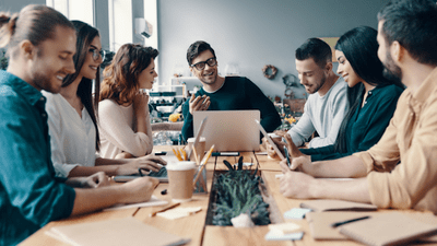 7 people sitting around a table in an official setting having a meeting